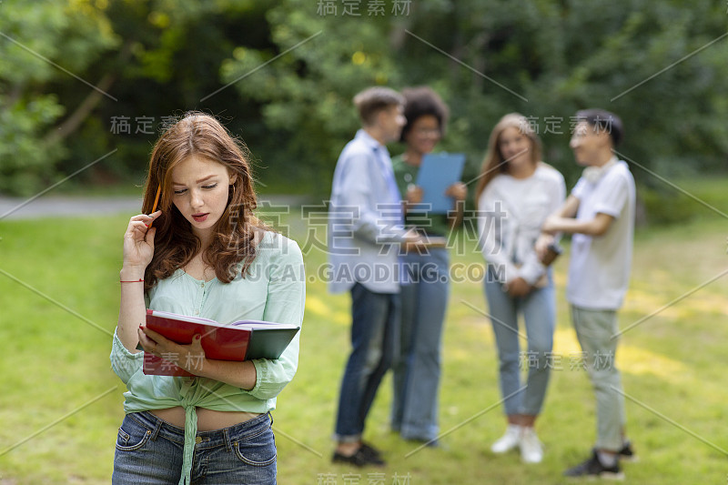 当她的同学们聊天时，一个专注的红发女学生在户外准备演讲