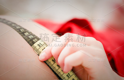 孕妇躺在床上，用黄黑相间的公制卷尺测量自己的腹部。年轻女人要生孩子了。