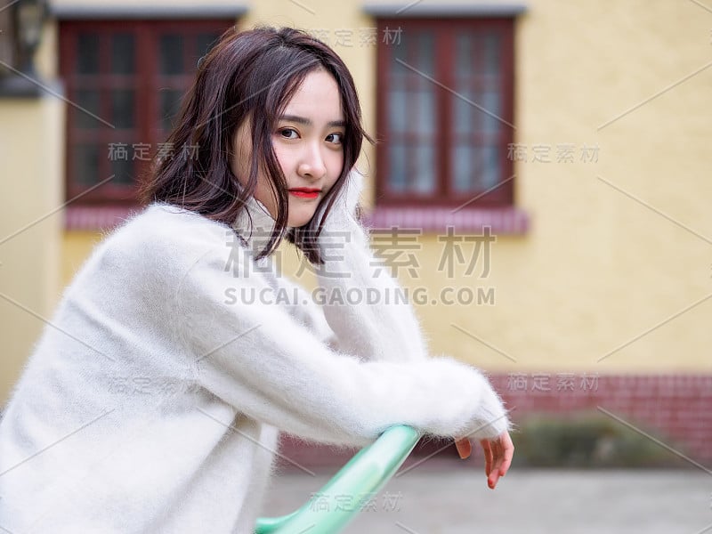 美丽年轻的黑发女人看着相机模糊的房子背景。户外时尚写真魅力中国年轻开朗时尚淑女，情感、人、美、生活理