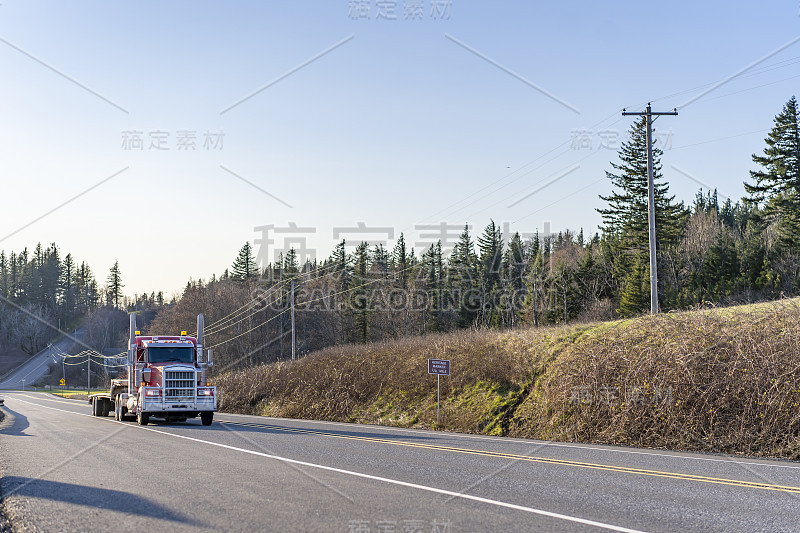 大型钻机强大的红色半挂车与铝格栅guard运行在道路与树木和山丘运输空步骤下半挂车