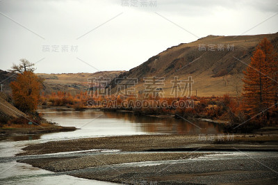 这条弯弯曲曲的河流流入了一个群山环绕的狭窄的秋季山谷。
