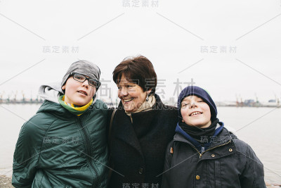 快乐的奶奶拥抱她的两个孙子在温暖的外套和帽子，微笑，看起来很愉快，感受爱和团聚