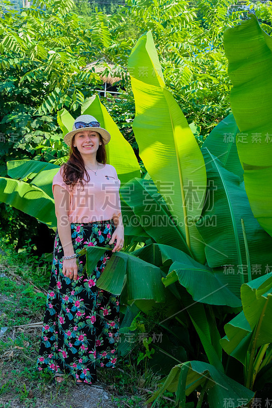 女孩肖像草帽，珊瑚色衬衫和热带印花裙。对着镜头笑得好。