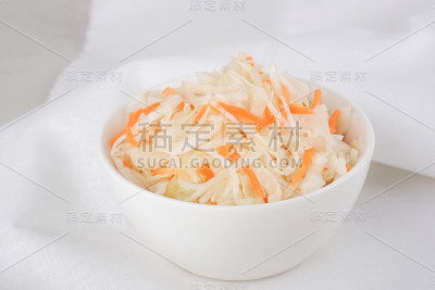 特写:在灰色背景下，白碗里的泡菜和胡萝卜。