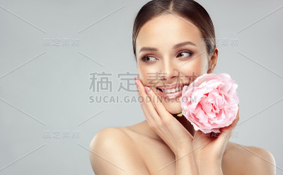 美丽的年轻女子捧着大朵淡玫瑰，面带温柔的微笑。自然的面部护理。