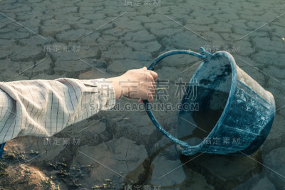 妇女双手在龟裂的地面上舀水，水短缺的概念。