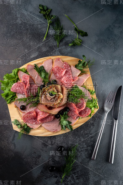 俯视图什锦切片美味的肉混合香肠，培根和火腿与欧芹和橄榄木砧板上灰色水泥背景与刀叉