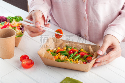 妇女吃蒸蔬菜在棕色的牛皮纸食品容器