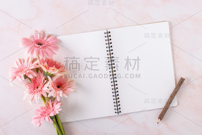顶视图的粉红色非洲菊花与笔记本和铅笔在大理石的背景。