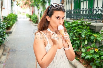 年轻漂亮的女人在一个阳光明媚的夏日假日里吃甜筒冰淇淋