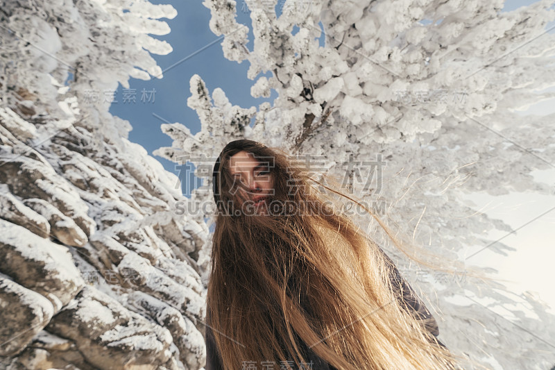 美丽的冬日画像下的年轻女子，白雪覆盖的杉树和悬崖，漂亮的微笑，长长的头发，阳光灿烂的冬日