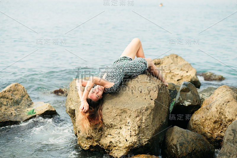 一个年轻美丽的女孩穿着大石头，风景如画的海边