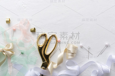 俯视图剪刀，彩色缎带，缝纫针，蝴蝶结，顶针在白色的缝纫桌上。设计空间