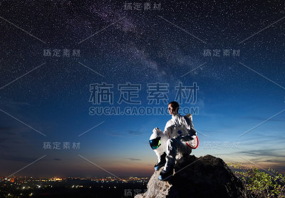 太空旅行者坐在岩石山在蓝天下。
