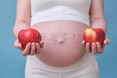 孕妇用两个红苹果，蓝色背景概念为怀孕两个孩子