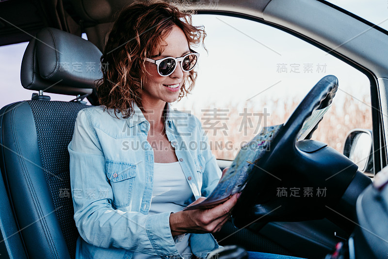 年轻漂亮的女人在车里看地图。旅游的概念