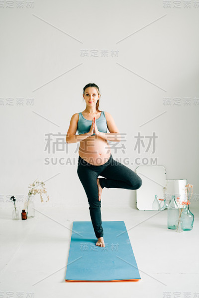一个年轻漂亮的孕妇穿着运动服在瑜伽室的垫子上做体式