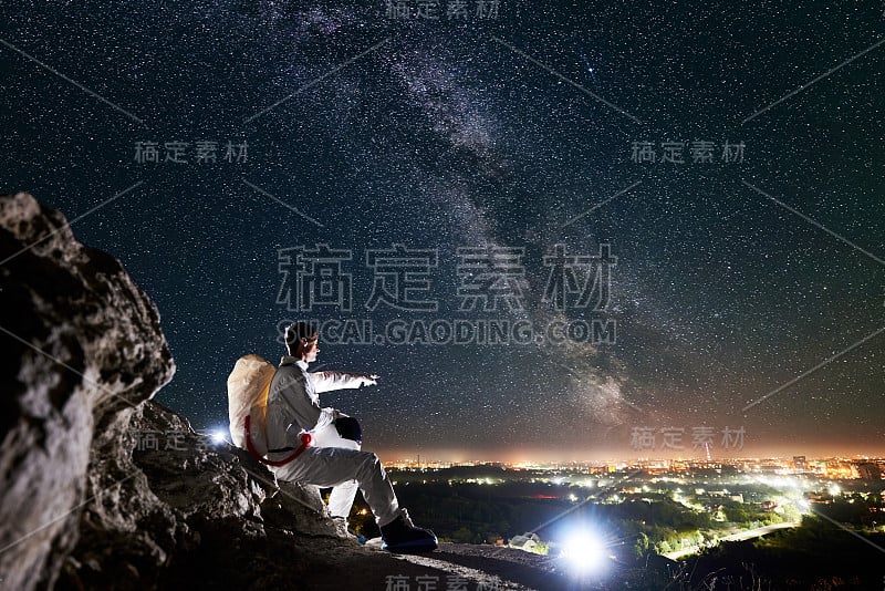 宇航员坐在布满星星的美丽夜空下的岩石山上。