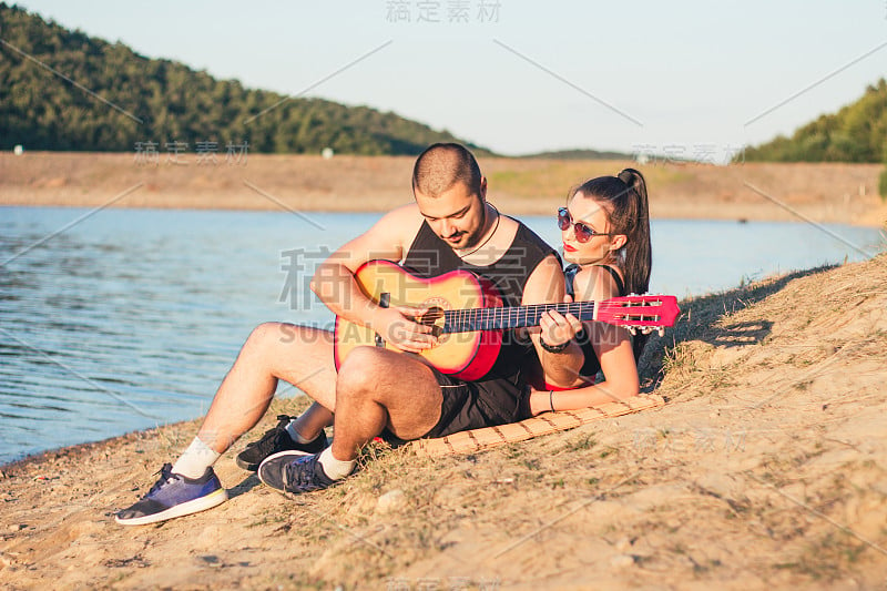 年轻男女在湖边拿着吉他。