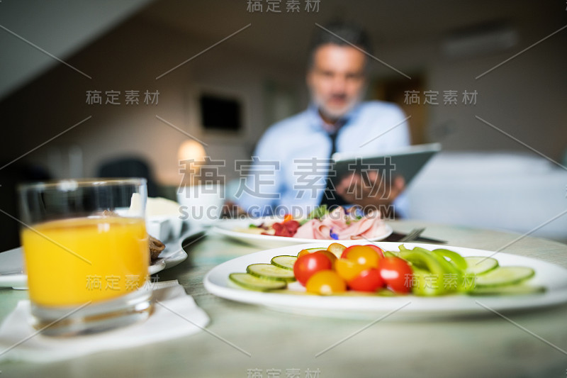 成熟的商人在酒店房间里拿着平板电脑。