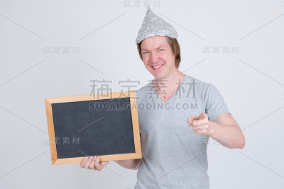 快乐的年轻人戴着锡纸帽，拿着黑板，指着相机