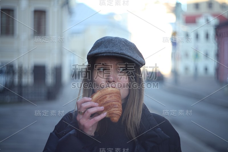 年轻漂亮的女孩在街上吃牛角面包