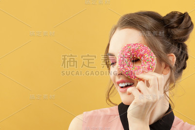 快乐的女人拿着甜甜圈在多彩的黄色背景，时尚肖像
