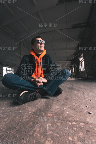 一名戴着墨镜的男子双腿交叉坐在水泥地板上