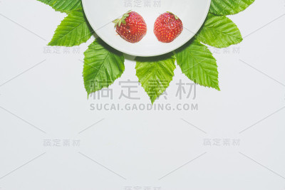 最小的草莓片背景。水果放在白色盘子里，周围是树叶。哑光色