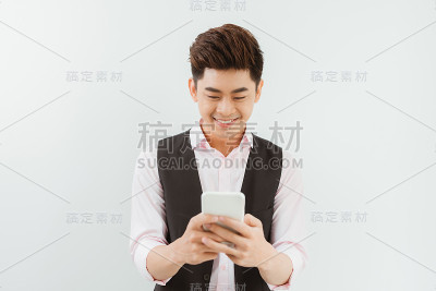 年轻的亚洲英俊商人微笑着阅读他的智能手机。