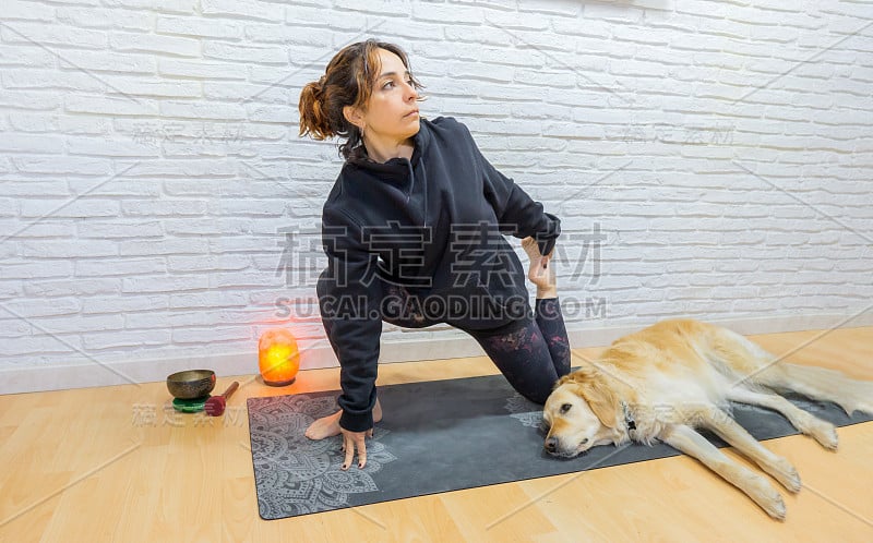 女孩在家里练习瑜伽，陪伴她的狗，一个非常有礼貌的金毛猎犬。