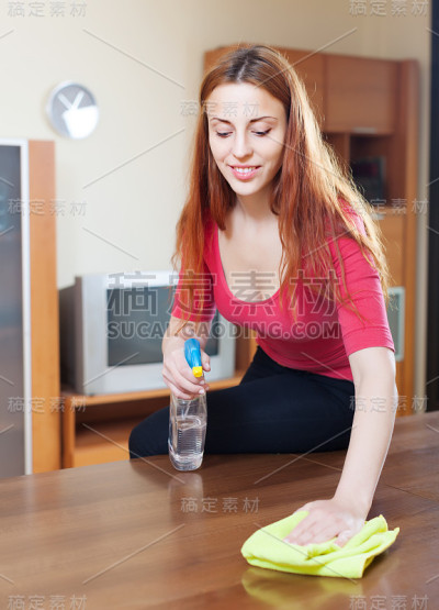 穿着红色衣服的女孩正在用家具上光剂擦拭桌子