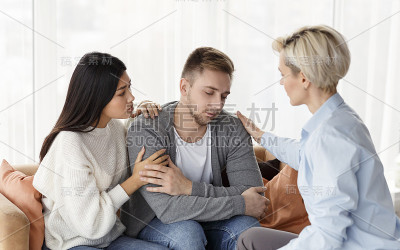 妻子和心理学家在室内心理治疗会议上安慰上瘾的丈夫