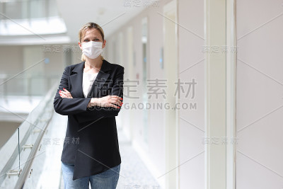 女商人戴着医用防护口罩，双臂交叉站在酒店走廊里