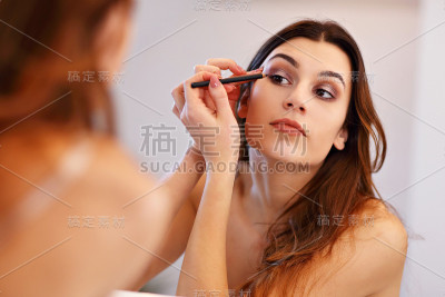 迷人的年轻女子化妆时，看着镜子在浴室