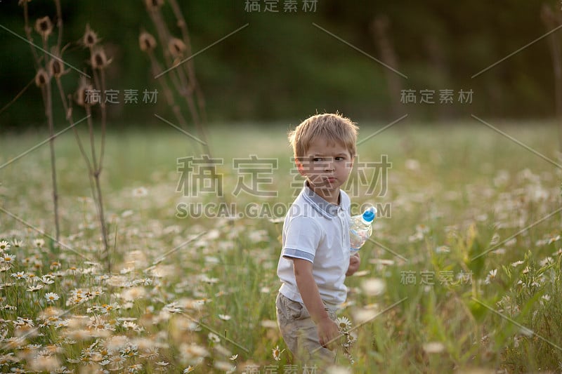 一个穿着白衬衫的小男孩走在春天盛开的绿色草地上