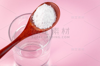 天然生物补充胶原蛋白粉在木勺和玻璃纯净水在粉红色的背景。概念健康皮肤和骨骼，抗衰老额外蛋白质产品。