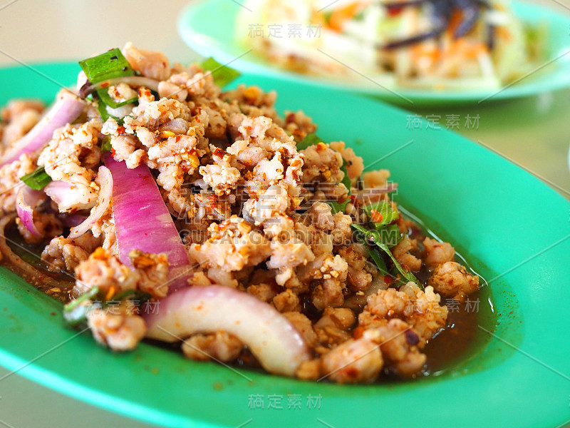 特写泰国当地的Larb Moo，一种生的香料炒猪肉，配上模糊的Som Tam