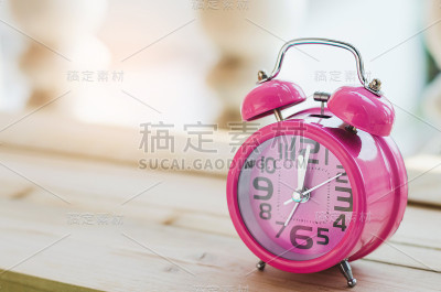 粉色复古闹钟在木板上与阳光。