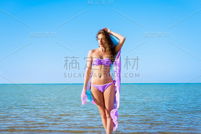 年轻美丽的女士与卷曲的头发摆姿势与帕雷奥在海滩上