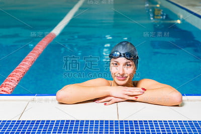 带着泳镜微笑的年轻女子在室内游泳池游泳