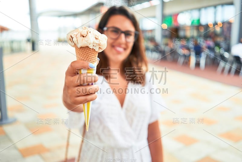 一个年轻漂亮的女人在一个阳光明媚的夏日假日在购物中心吃冰淇淋蛋筒