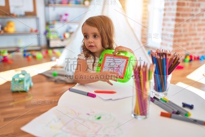 可爱的金发幼童使用数字板周围的许多玩具在幼儿园