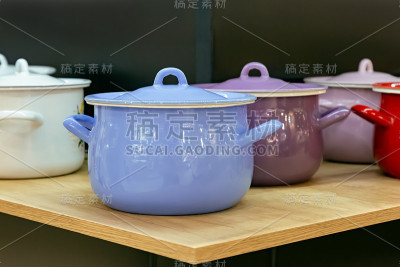 厨房的架子上放着许多漆包钢金属的彩色新式烹饪锅。家居用品、餐具、厨房用具。商店橱窗，销售国内产品，室