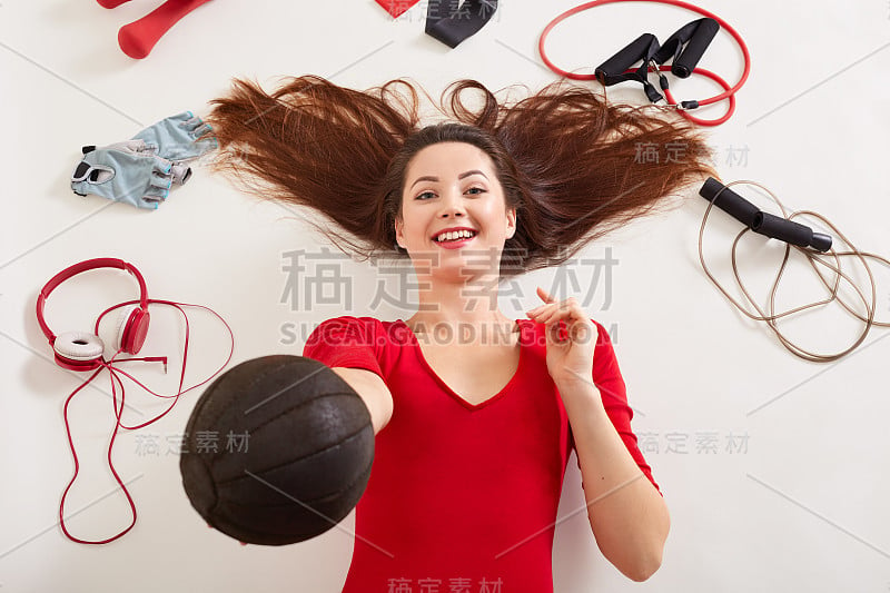 特写美丽快乐的女运动员与medball在手中，女性包围耳机，跳绳，健身手套，橡皮筋，扩张器，在健身房