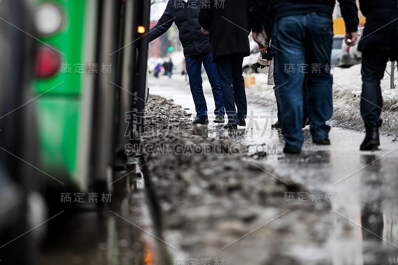 人们站在公共汽车站上公共汽车，踩着未清理的雪和泥，特殊服务不能清洁城市