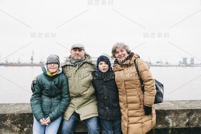 爷爷奶奶和孙子们穿着冬衣站在水边，微笑着，拥抱着，幸福地在一起