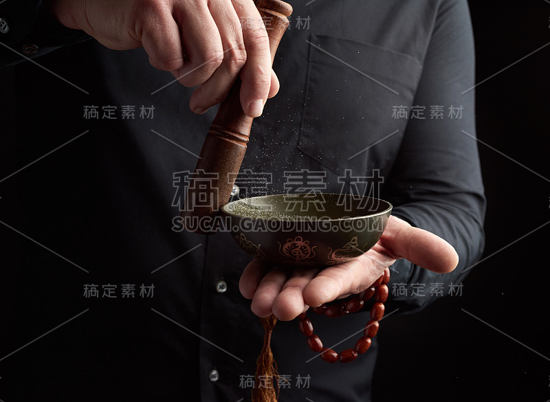 一名身穿黑色衬衫的成年男子在一个藏铜碗周围旋转一根木棍。仪式的冥想