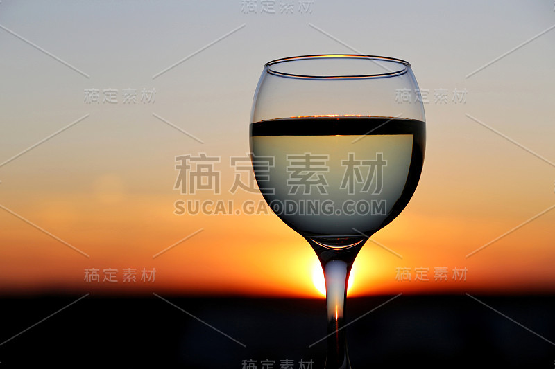 在美丽的夕阳背景下，一杯白葡萄酒，阳光透过酒杯的茎