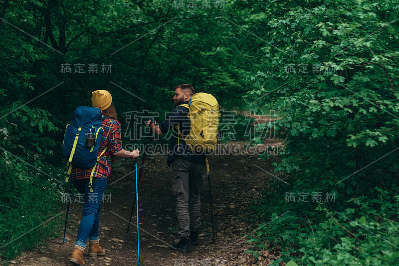 一对年轻的徒步旅行者使用登山杖和背着背包